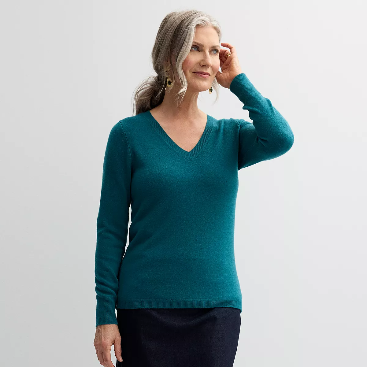 A woman is wearing a teal v-neck sweater with long sleeves and ribbed cuffs and hem over a dark skirt.