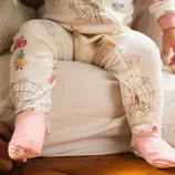 A baby wearing a cream-colored onesie with carnival-themed graphics and pink socks.