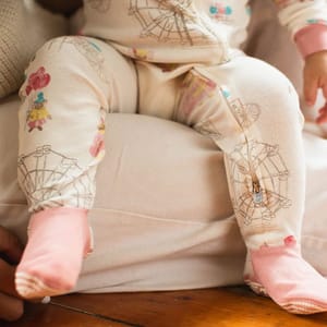 A baby wearing a cream-colored onesie with carnival-themed graphics and pink socks.