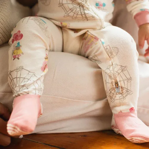 A baby wearing a cream-colored onesie with carnival-themed graphics and pink socks.
