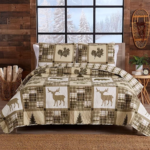 A rustic bed set featuring a quilt and pillowcases with a woodland theme, including deer, trees, and plaid patterns, set in a cozy cabin-style room with a snowy window view and wooden accents.