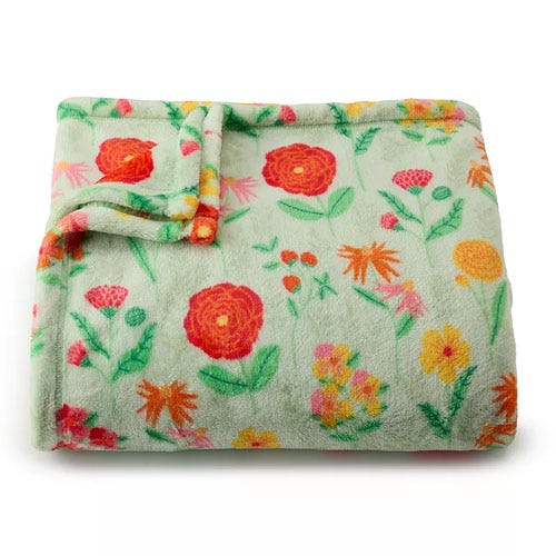 A soft, folded blanket with a floral print featuring red, orange, and yellow flowers on a light green background.