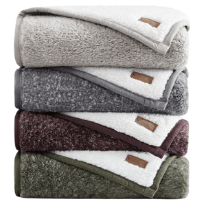 A stack of four plush sherpa-lined blankets in neutral colors: beige, gray, dark red, and olive green. Each blanket features a stitched label.