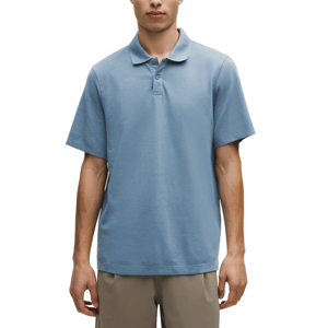 A man is wearing a light blue short-sleeve polo shirt paired with beige trousers. The shirt features a classic collar and button details.