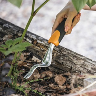 Hand using a garden weeder to remove weeds from soil.