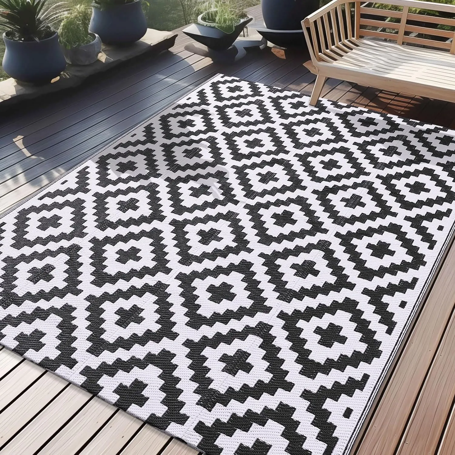 Black and white outdoor rug with a geometric diamond pattern, measuring 5' x 8', placed on a patio next to a wooden bench and potted plants.