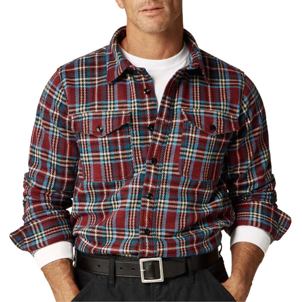 A man wears a red, blue, and white plaid flannel shirt over a white T-shirt, paired with a black belt and dark pants.