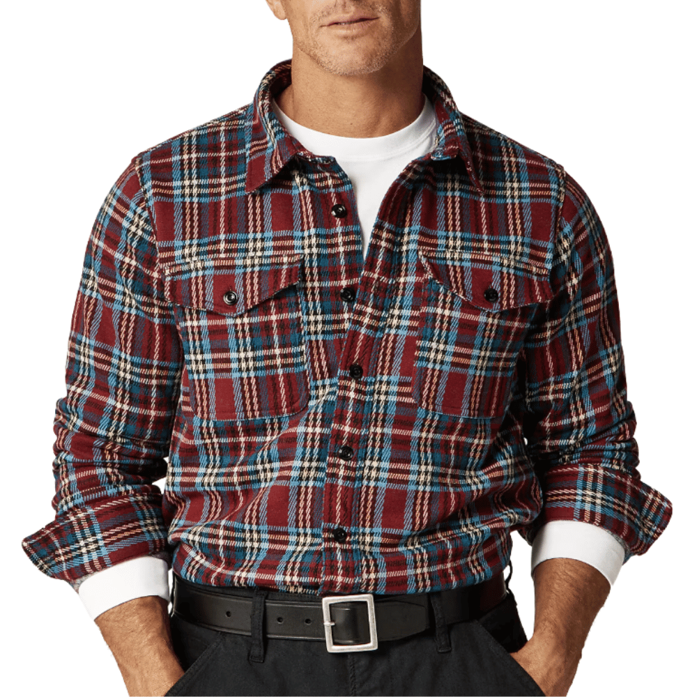 A man wears a red, blue, and white plaid flannel shirt over a white T-shirt, paired with a black belt and dark pants.