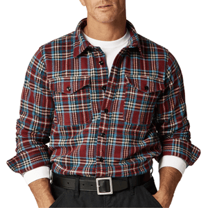 A man wears a red, blue, and white plaid flannel shirt over a white T-shirt, paired with a black belt and dark pants.