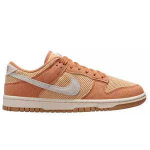 A Nike Dunk Low sneaker in shades of peach and orange with a light gray swoosh, featuring a textured design and a rubber sole.