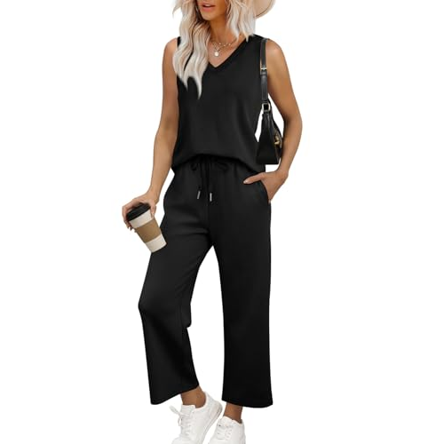 A woman is wearing a sleeveless black jumpsuit with a V-neck and drawstring waist, paired with white sneakers and a black shoulder bag. She's holding a coffee cup and wearing a wide-brimmed hat.