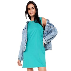 A woman wearing a sleeveless turquoise dress and a blue denim jacket draped over her shoulders.