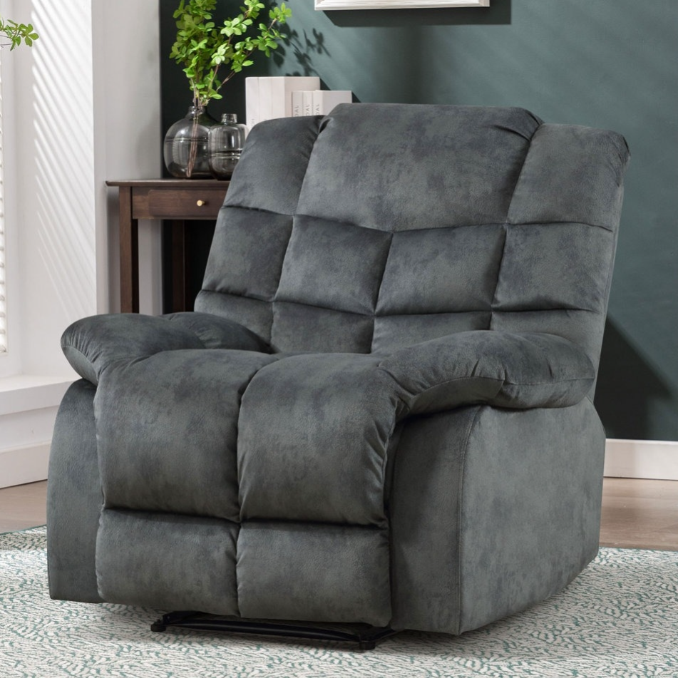 A plush, gray reclining armchair is set against a dark green wall, with a light rug beneath it and a small wooden side table with books and decorative items nearby.