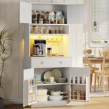 A kitchen cabinet displays glass jars, a coffee machine with mugs hanging above, and lower shelves with dishes and cookware. The doors hold spices and snacks. A dining table is partially visible in the background.