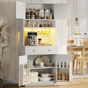 A kitchen cabinet displays glass jars, a coffee machine with mugs hanging above, and lower shelves with dishes and cookware. The doors hold spices and snacks. A dining table is partially visible in the background.