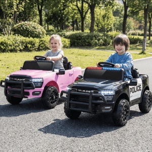 Two children are riding toy RAM trucks, one pink and the other black with police markings, in an outdoor setting.