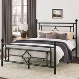 Black metal bed frame with decorative design, set in a room with a white rug, wooden nightstand, lamp, and gray curtains.