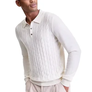 A man wears a cream-colored, cable-knit sweater with a collar and button placket, paired with light-colored trousers.