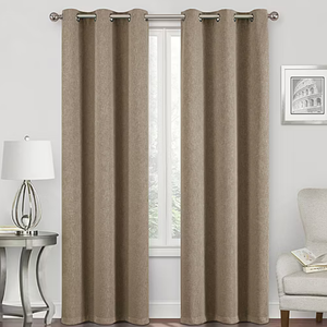 Neutral-colored curtains with eyelet rings hang on a rod in front of a window, accompanied by a contemporary lamp on a side table and a framed picture on the wall.