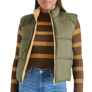 Steve Madden Reversible Puffer Vest features a green exterior with a light yellow interior, a high collar, and sleeveless design, paired with a brown and yellow striped sweater and blue jeans.