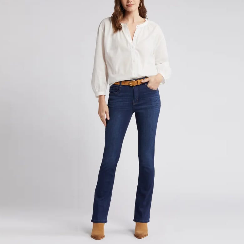 A woman is wearing dark blue jeans, a white blouse, and a brown belt.