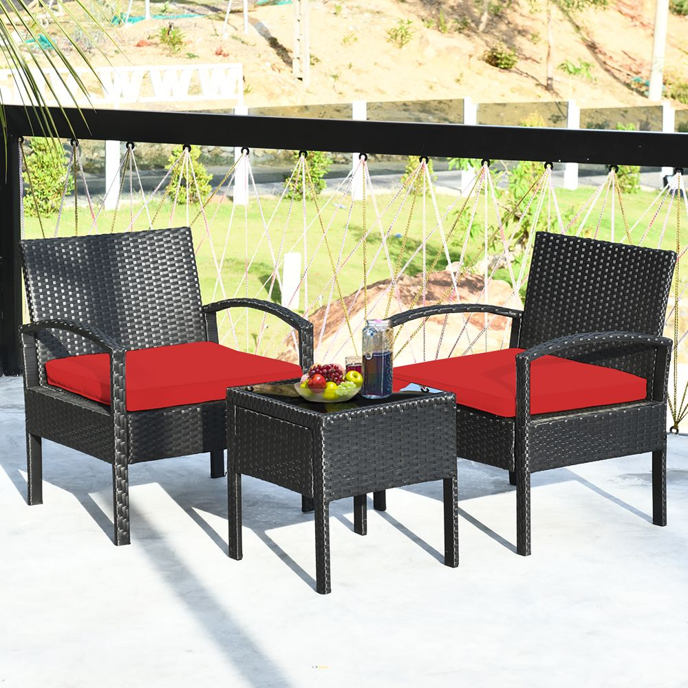 Rattan patio furniture set with two armchairs featuring red cushions and a small glass-top side table, placed outdoors on a balcony.