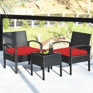 Rattan patio furniture set with two armchairs featuring red cushions and a small glass-top side table, placed outdoors on a balcony.