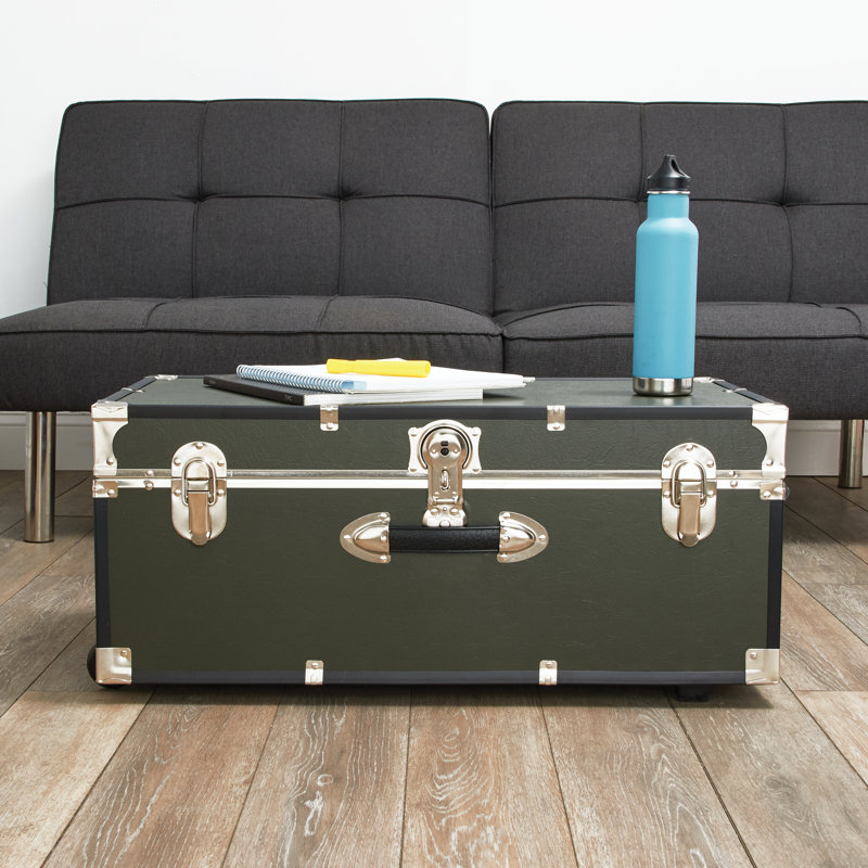 Dark gray sofa and a trunk with metal accents, featuring a notebook, pen, and blue water bottle on top.