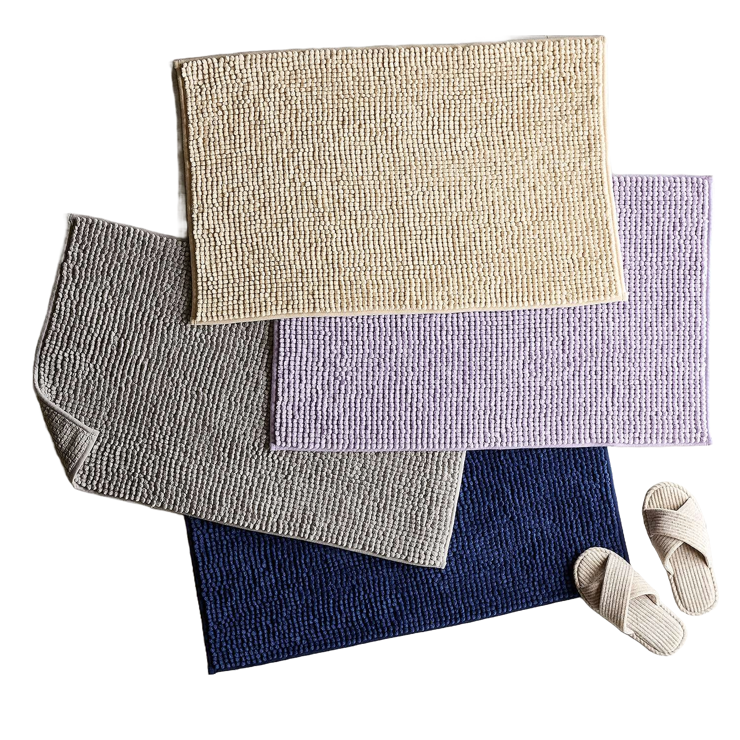 Four textured bath mats in beige, gray, lavender, and dark blue are layered together, accompanied by a pair of light-colored slippers.