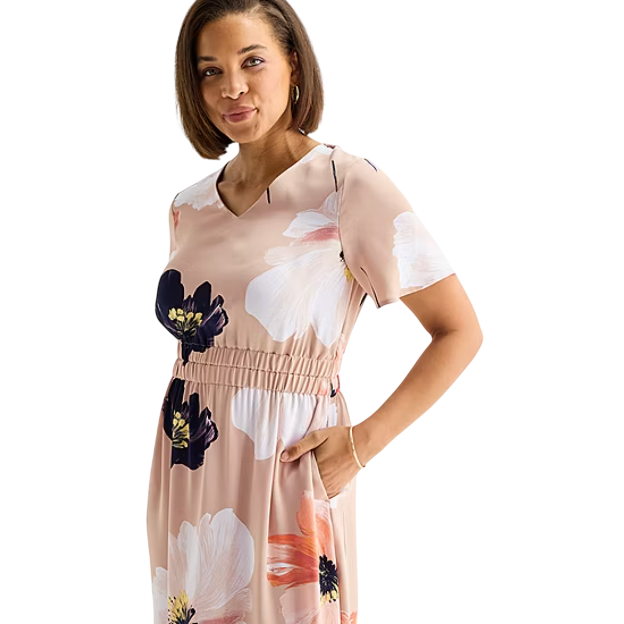 A woman wears a beige dress with large floral patterns in white, black, and orange, featuring short sleeves, a V-neck, an elastic waist, and side pockets.