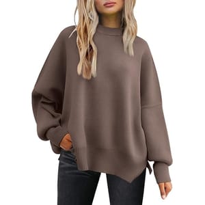 A woman models an oversized brown ribbed sweater paired with dark jeans. The sweater features a high neckline and dropped shoulders.