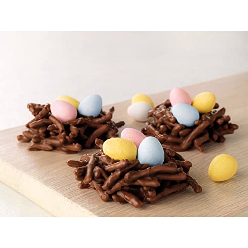 Three chocolate nests are filled with colorful candy eggs, displayed on a wooden board.