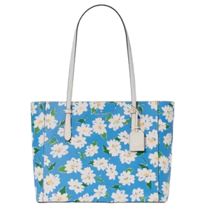 A blue Kate Spade tote adorned with a white floral print features long white handles and an attached tag.