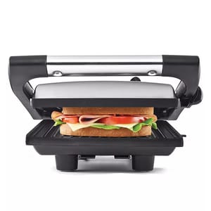A panini press and sandwich grill featuring a stainless steel top, black handle, and grill plates, shown pressing a sandwich with lettuce, tomato, cheese, and meat.