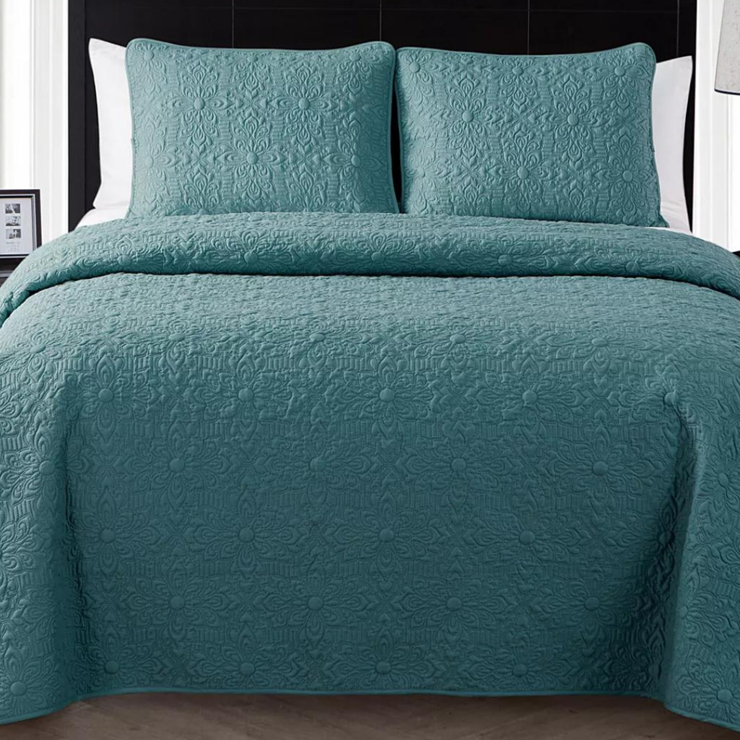 A teal quilted bedspread with matching pillows on a bed.