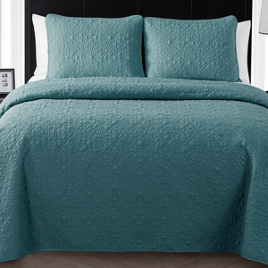 A teal quilted bedspread with matching pillows on a bed.