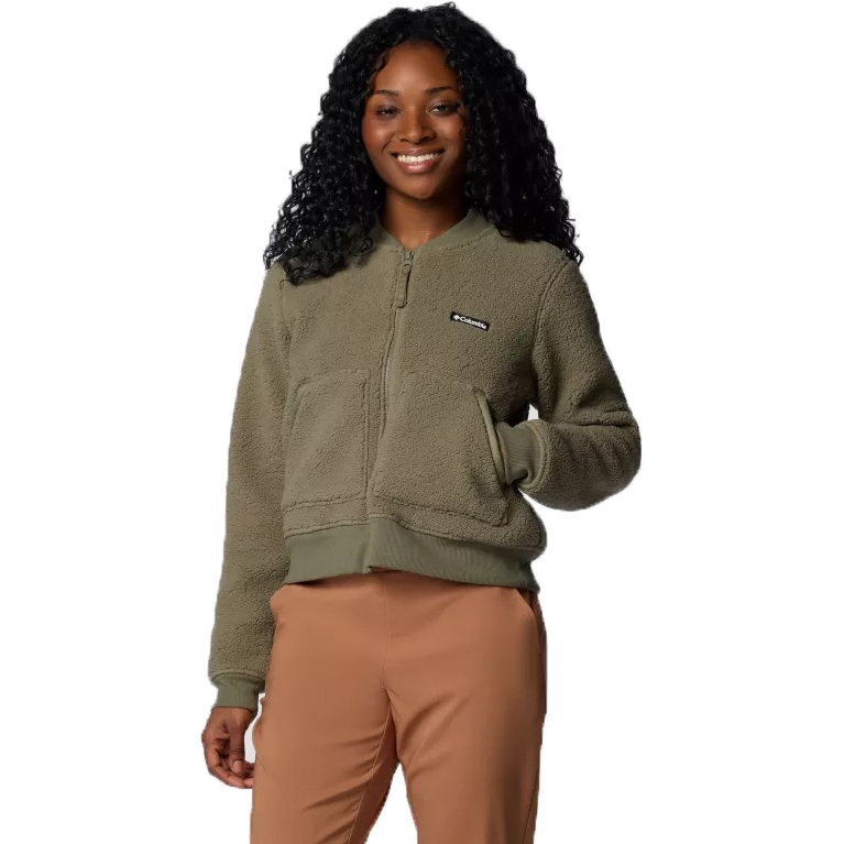 A woman is wearing a green Columbia bomber jacket with a full front zipper and a small logo on the left chest, paired with tan pants.
