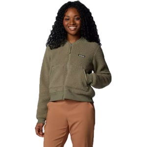 A woman is wearing a green Columbia bomber jacket with a full front zipper and a small logo on the left chest, paired with tan pants.