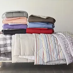 Stacked comforters in various colors and patterns displayed on a bed.