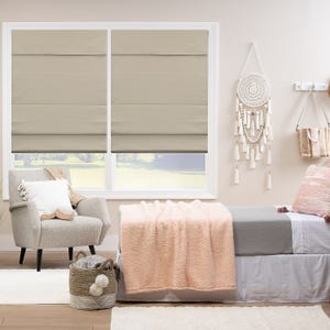 Roman shades on windows, a beige armchair, and a daybed with a pink blanket in a well-lit room.