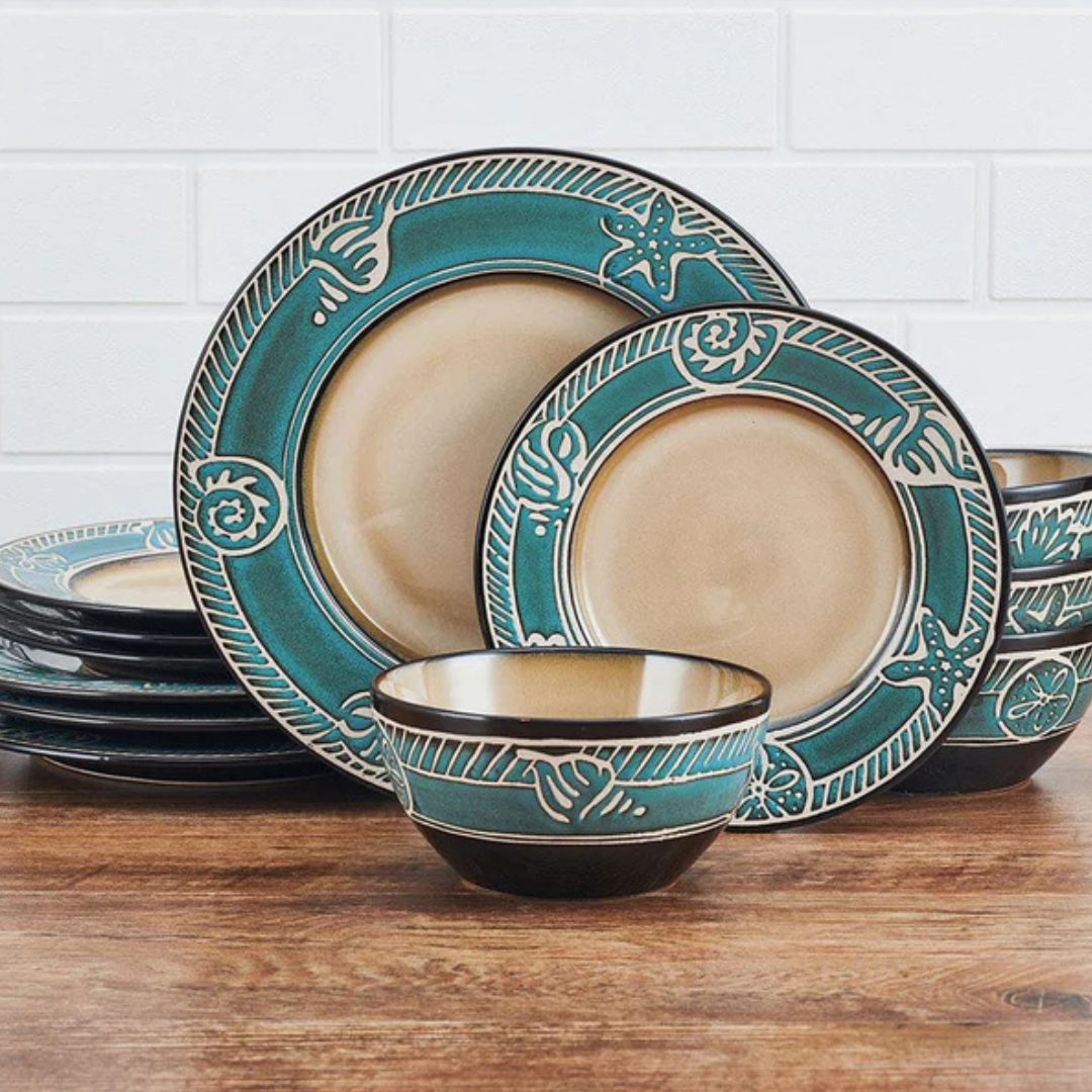 A set of ceramic dinnerware featuring plates and bowls with a turquoise and beige seashell and starfish design on the rims, arranged on a wooden surface against a tiled wall background.
