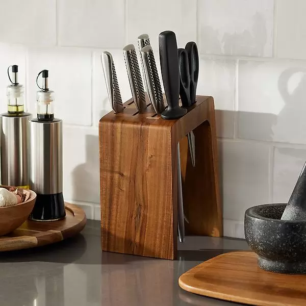 Acacia wood knife block with slots for knives and scissors, featuring a sleek, modern design. It's paired with stainless steel and black-handled tools, set on a kitchen countertop alongside oil dispensers and a mortar and pestle.