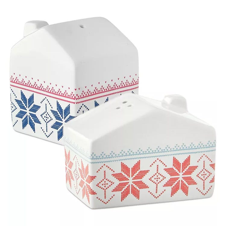The Cellar Holiday Salt & Pepper Shaker set features two ceramic house-shaped shakers, each adorned with a festive cross-stitch pattern—one in red and the other in blue.