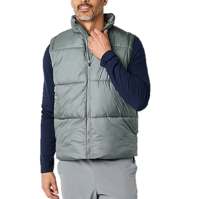 A man wears a light gray quilted athletic vest with a zip front over a navy long-sleeve shirt. The vest has horizontal stitching and a high collar, providing a casual and sporty look.