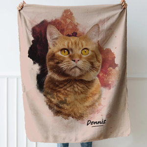 A person holds a blanket featuring a realistic print of an orange tabby cat with striking yellow eyes and a watercolor background. The name \“Dennis\“ is printed at the bottom.