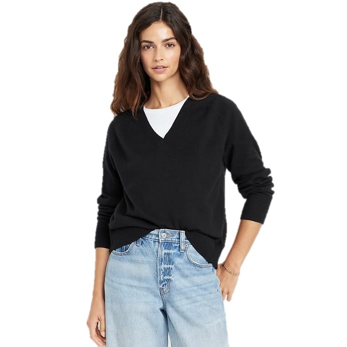 A woman is wearing a loose-fitting black V-neck sweater with ribbed cuffs over a white top, paired with light blue jeans.