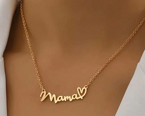 A gold necklace featuring the word \“Mama\“ in cursive script, adorned with a heart symbol at the end, hanging on a delicate chain around the neck.