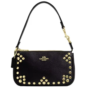 A black Coach Outlet Nolita bag with gold-tone studs accenting the front, featuring a detachable leather strap and gold hardware. The Coach logo is prominently displayed on the front.