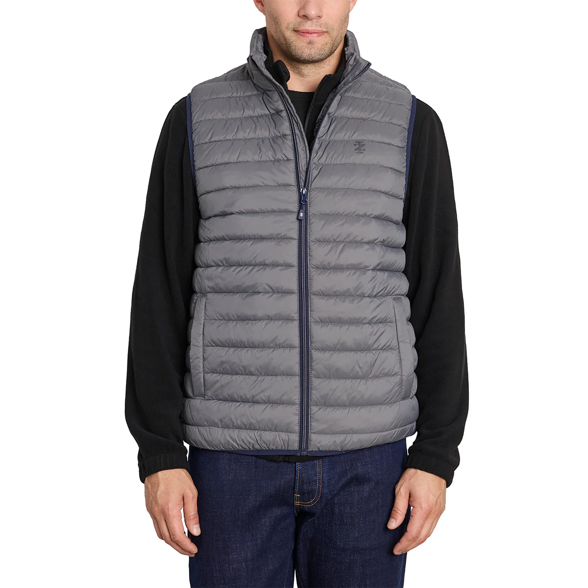 A man is wearing a gray quilted puffer vest over a black long-sleeve shirt paired with blue jeans.