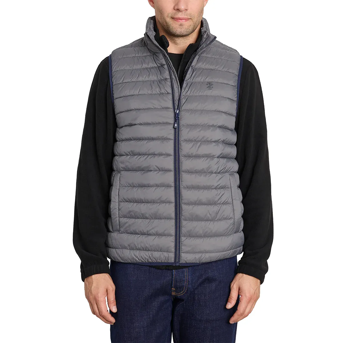A man is wearing a gray quilted puffer vest over a black long-sleeve shirt paired with blue jeans.
